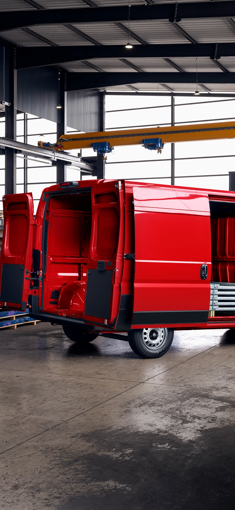 Vista trasera tres cuartos de una Citroën Jumper roja con puertas de carga abiertas dentro de una nave, destacando el gran espacio de carga, durabilidad y versatilidad profesional.