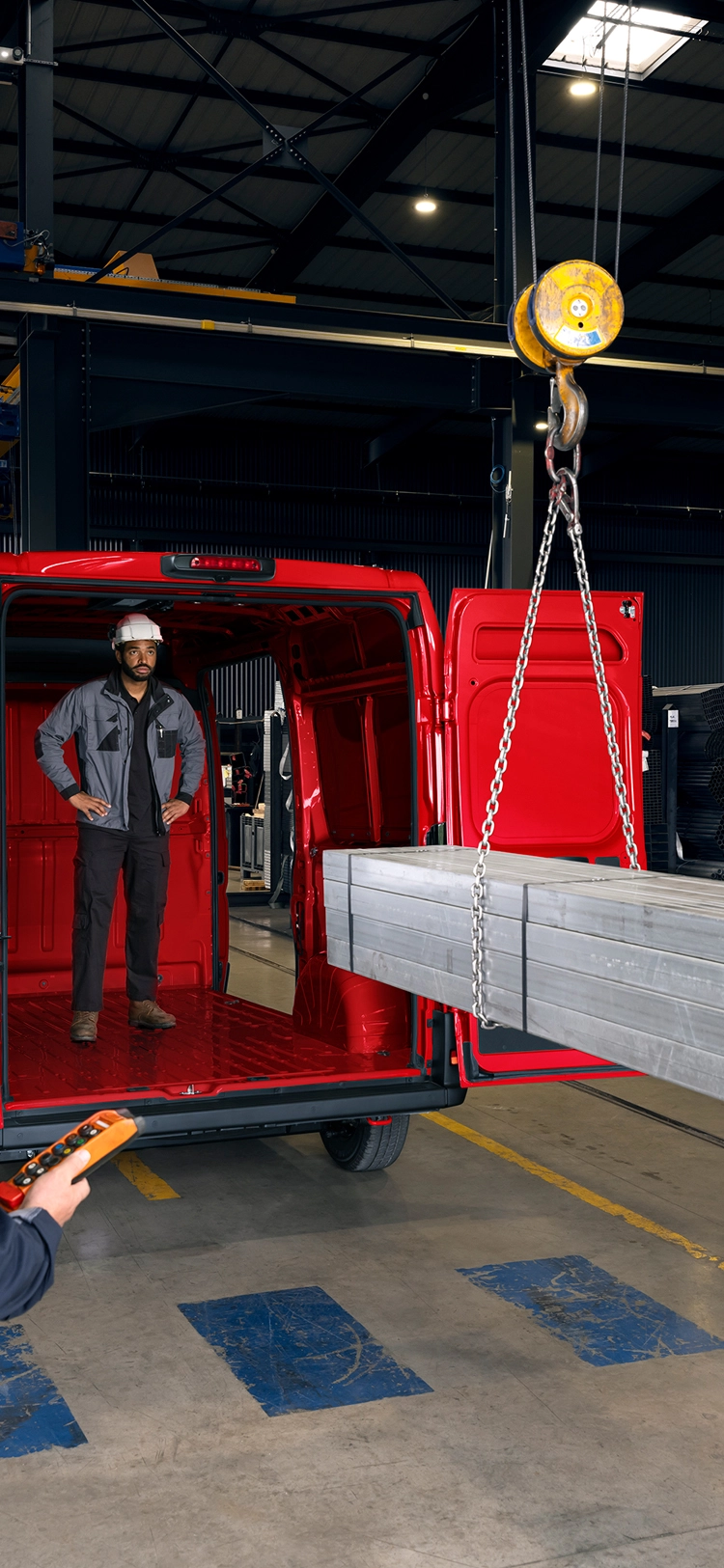Vista trasera de una Citroën Jumper roja siendo cargada con vigas metálicas en un entorno industrial, destacando el gran volumen de carga y capacidad para trabajo pesado.