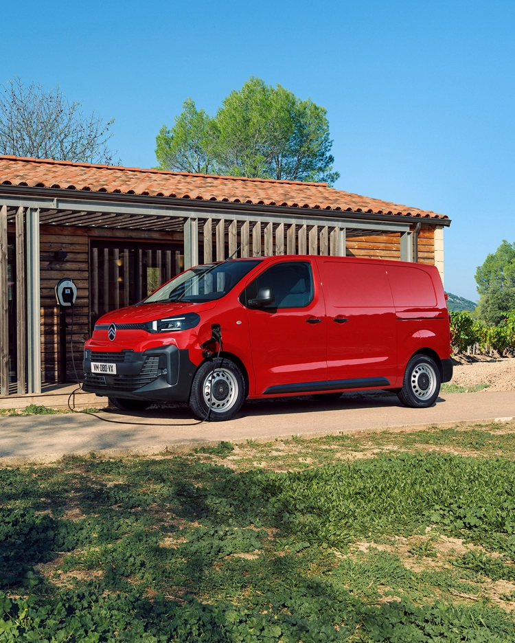 Vista exterior tres cuartos lateral de un Citroën ë-Jumpy rojo cargando frente a un edificio, mostrando diseño eléctrico moderno, practicidad diaria, conectividad y presencia profesional segura.
