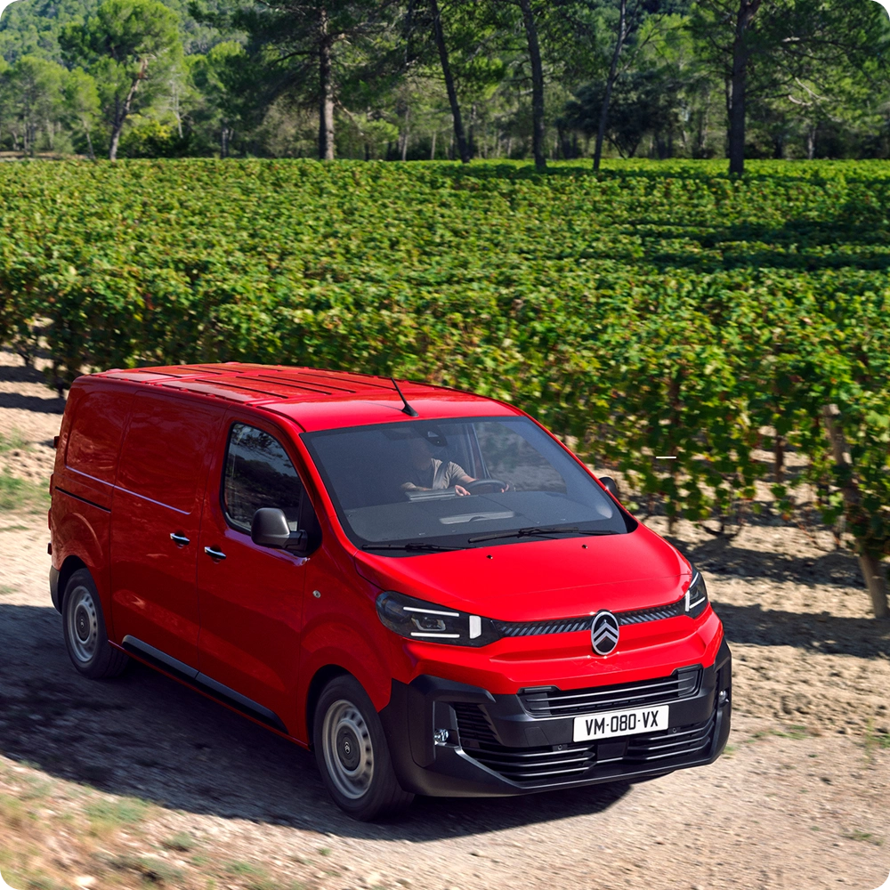 Vista exterior frontal tres cuartos de un Citroën Jumpy rojo circulando en un entorno urbano, mostrando funciones de seguridad, confort de conducción y presencia profesional segura.
