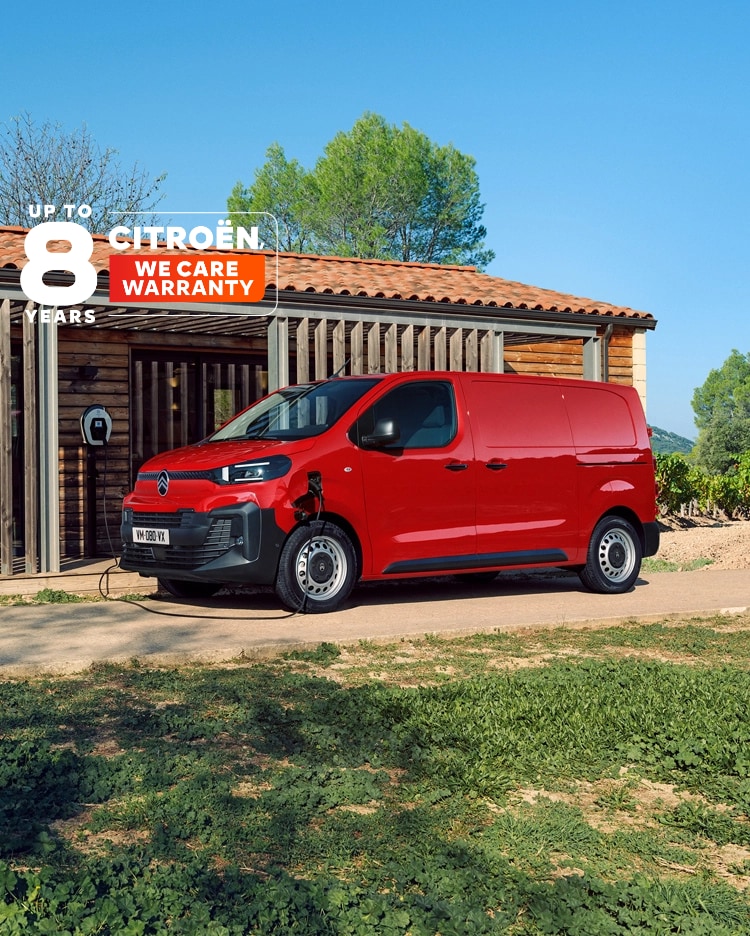 Vista exterior tres cuartos lateral de un Citroën ë-Jumpy rojo cargando frente a un edificio, mostrando diseño eléctrico moderno, practicidad diaria, conectividad y presencia profesional segura.