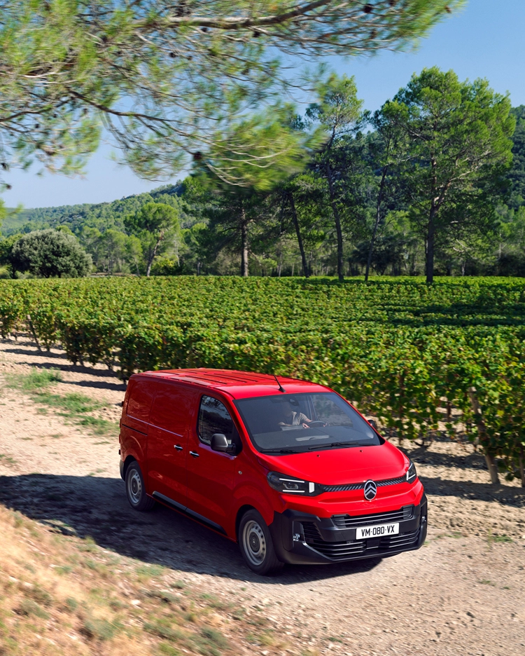 Three‑quarter front view of a red Citroën Jumpy driving on a rural road, showing robust design, driving comfort, versatility and confident presence.