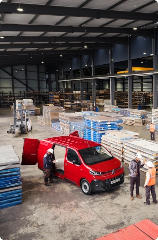 Vista exterior en ángulo alto de un Citroën Jumpy rojo aparcado en un almacén industrial, mostrando dimensiones exteriores compactas, gran capacidad de carga y practicidad profesional.