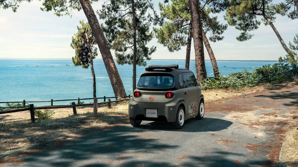 Vista trasera tres cuartos del Citroën Ami Outdoor junto a la costa, con techo abierto para disfrutar del tiempo libre.