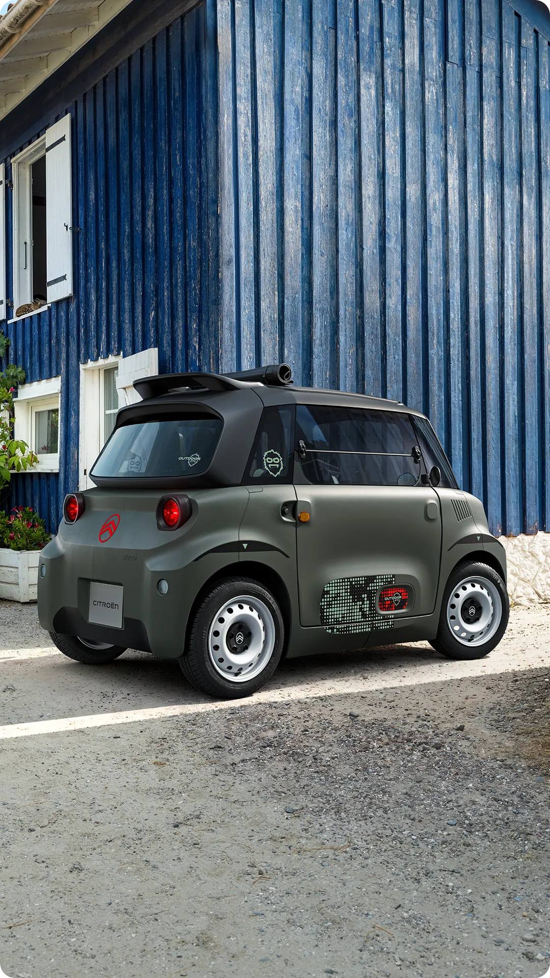 Vista frontal del Citroën Ami Outdoor con faros LED, un vehículo eléctrico ultracompacto circulando por una calle estrecha.