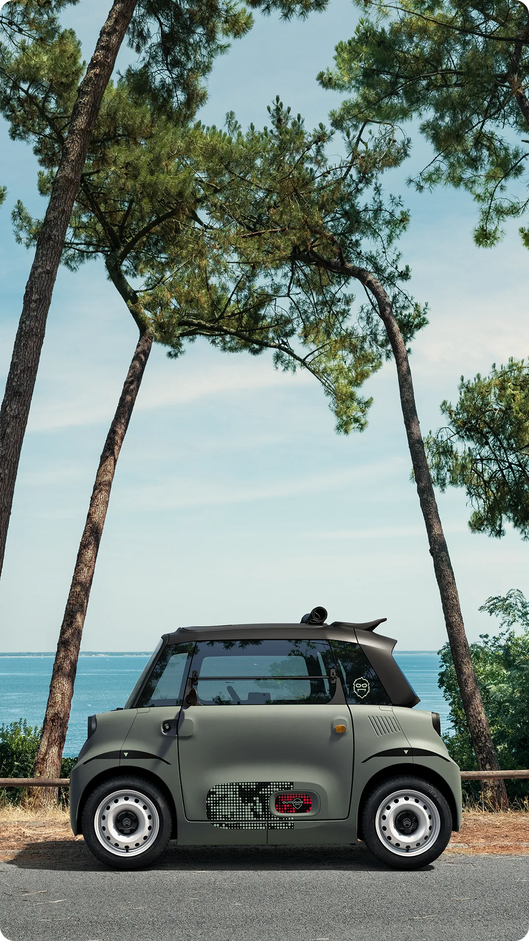 Vista de perfil del Citroën Ami Outdoor con el techo abierto junto a la costa, ideal para los desplazamientos de ocio.