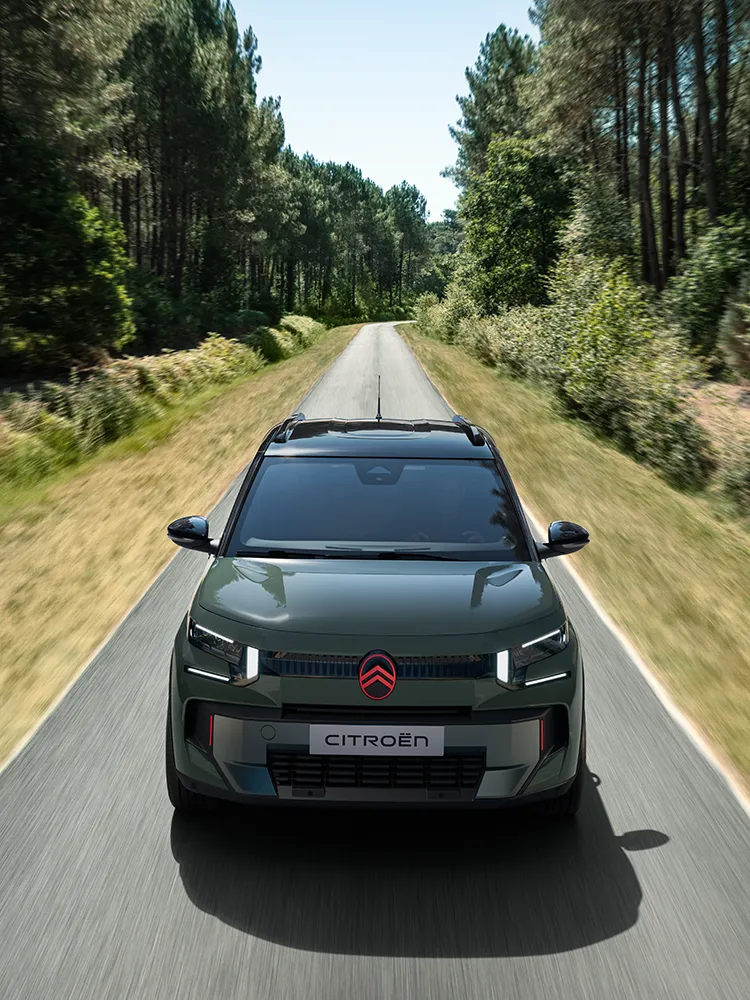 Vista frontal elevada del Citroën ëC3 Outdoor, con firma luminosa LED y Advanced Comfort, en una carretera entre bosques