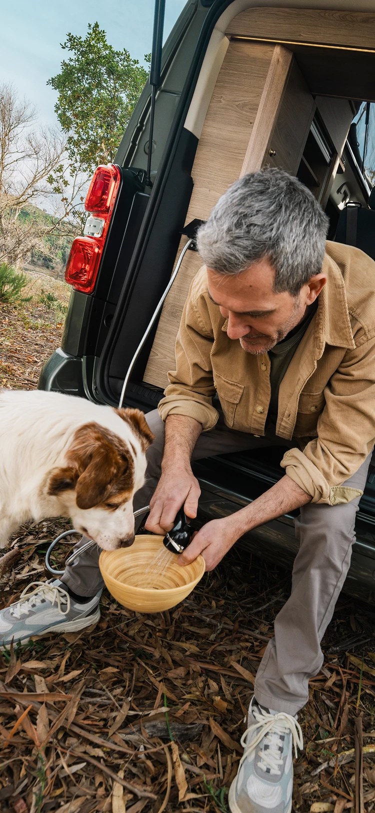 Hombre dando de comer a un perro desde la parte trasera de una furgoneta camper Citroën en un entorno al aire libre