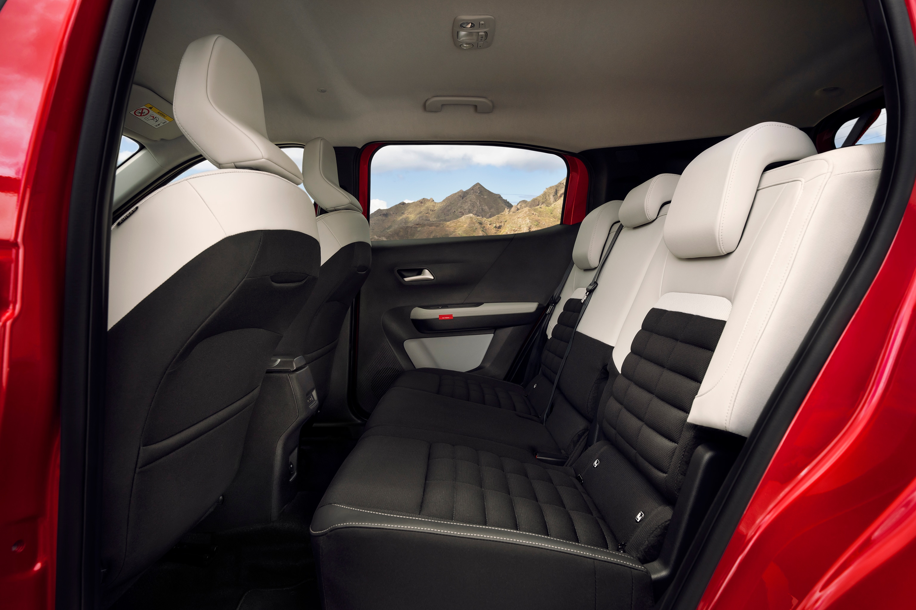 Vista de los asientos traseros del Citroën ë-C3 Aircross SUV compacto con tapicería negro y blanco y vista de montaña exterior.