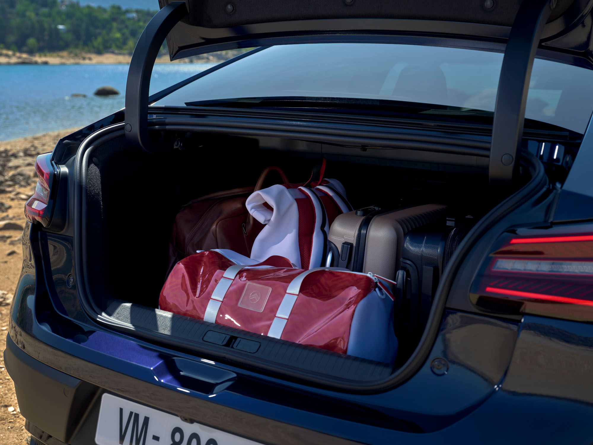 Maletero abierto del Citroën C4 X cargado con bolsas de viaje junto a una ubicación lacustre.