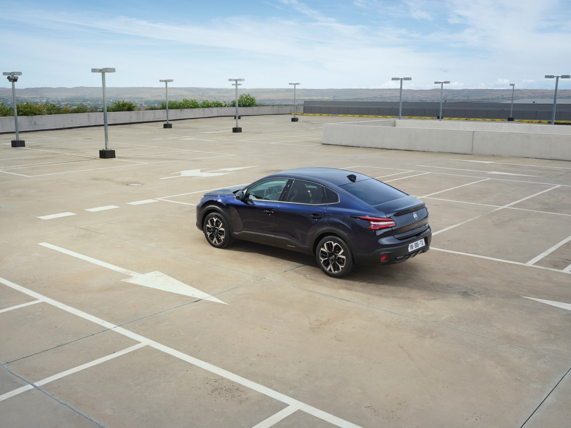 Vista trasera tres cuartos del Citroën C4 X en parking de azotea abierto destacando líneas fastback elegantes para una movilidad asequible.