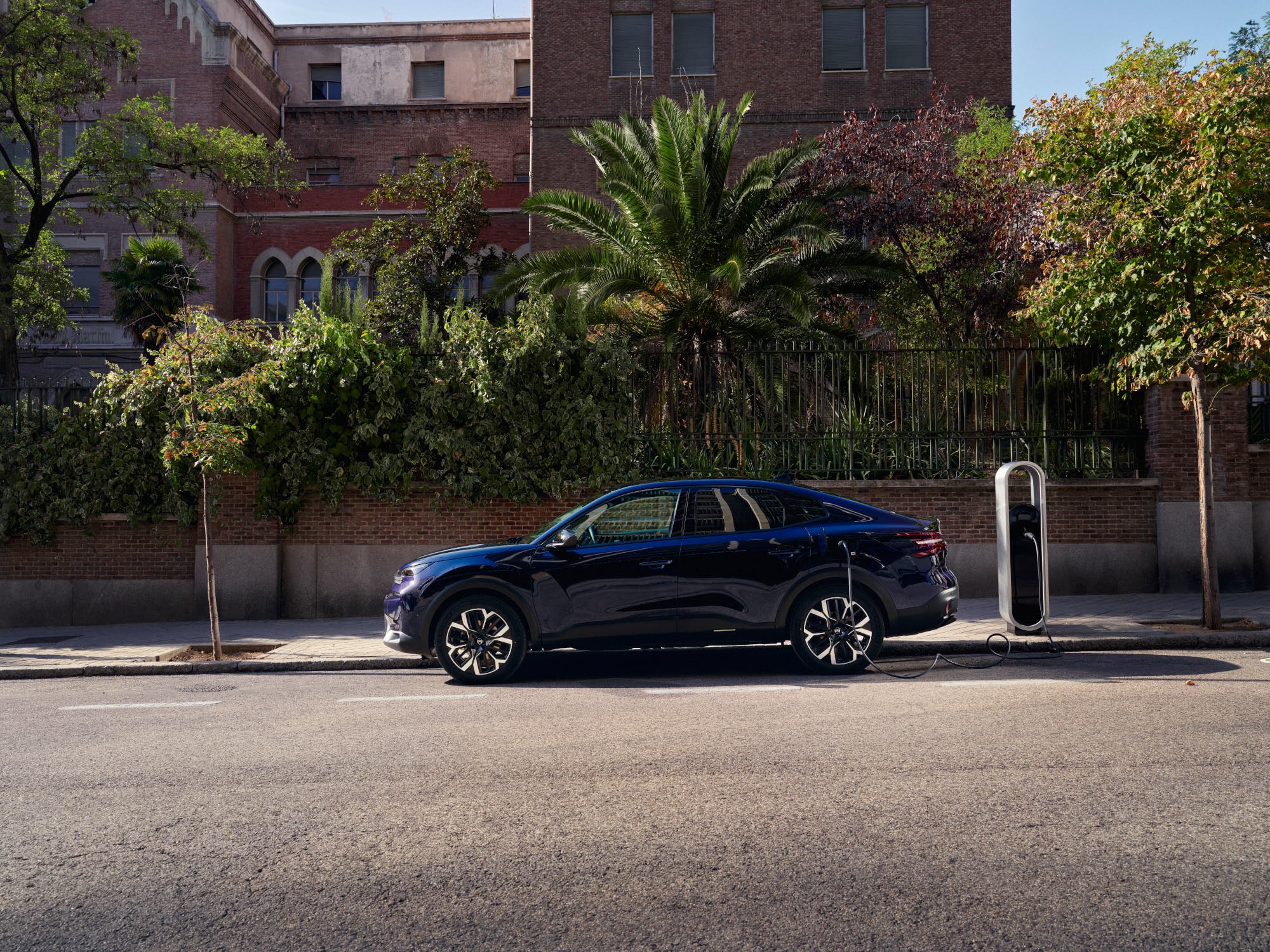 Vista lateral del Citroën C4 X fastback eléctrico cargando en la calle, destacando movilidad urbana conveniente y asequible.
