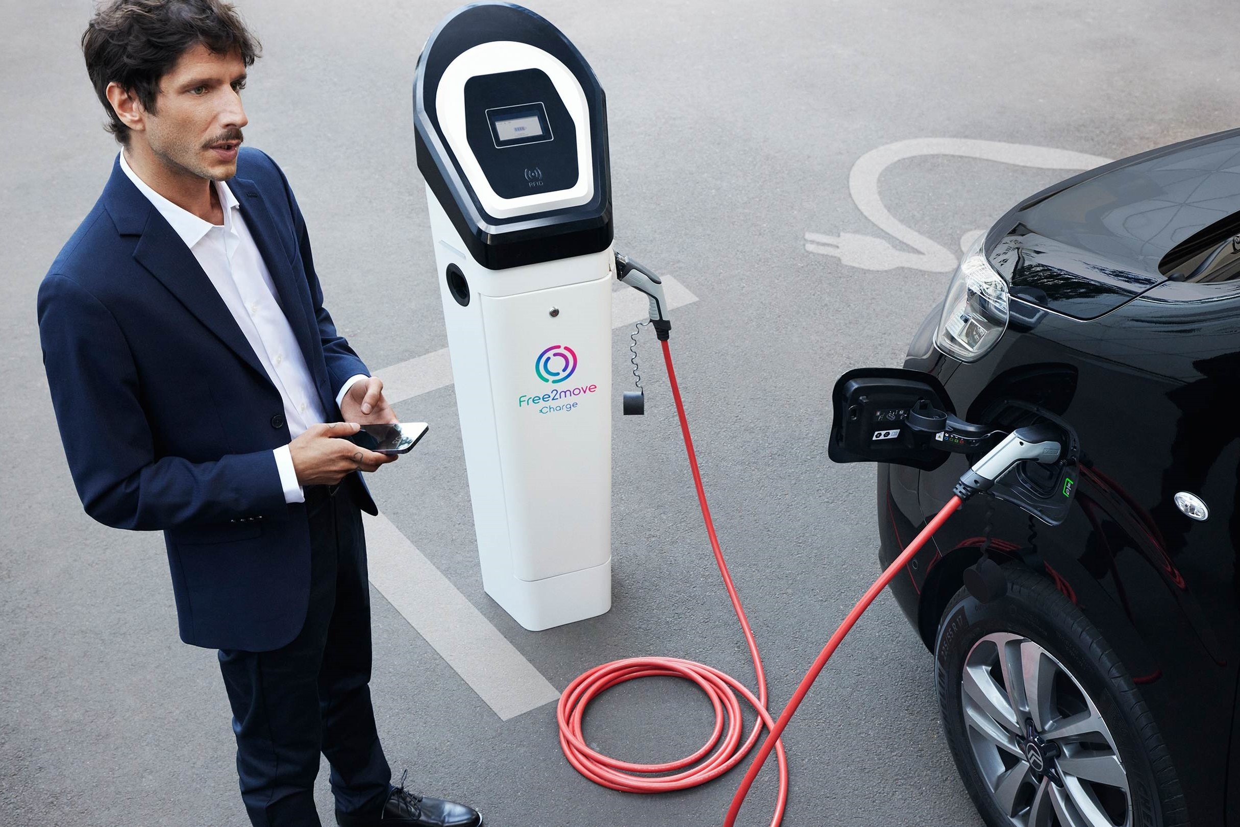 Vehículo eléctrico cargando en una estación pública mientras se usa una app del smartphone para gestionar la carga con Free2move Charge